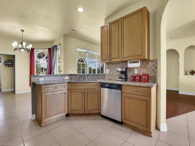 Kitchen featuring an inviting chandelier, stainless steel dishwasher, light tile patterned floors, tasteful backsplash, and a sink