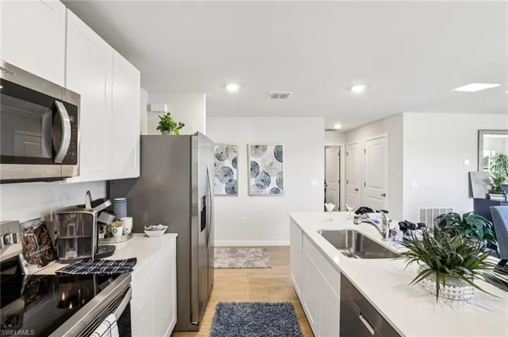 Model home. Kitchen with stainless steel appliances, white cabinets, light wood-type flooring, and recessed lighting