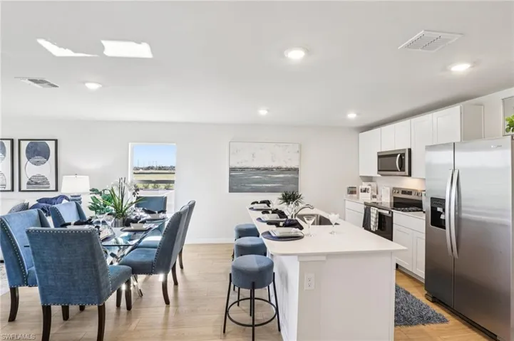 Model home. Kitchen with stainless steel appliances, white cabinets, a breakfast bar area, light wood-style floors, and a center island with sink