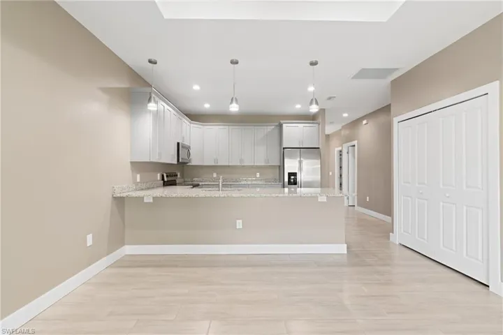 Kitchen featuring appliances with stainless steel finishes, white cabinets, sink, kitchen peninsula, and light stone counters