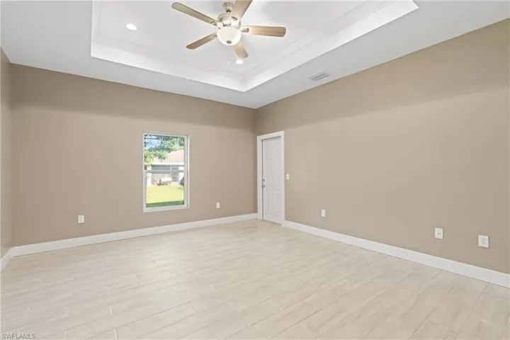 Empty room featuring a raised ceiling, ornamental molding, and ceiling fan