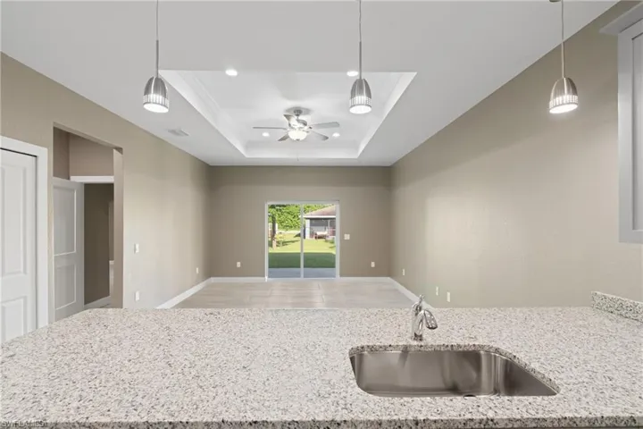 Kitchen featuring wood-type flooring, ceiling fan, a tray ceiling, sink, and light stone countertops