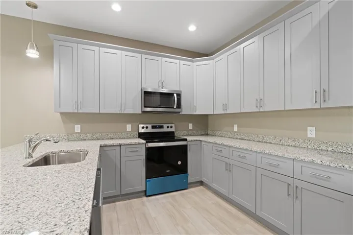 Kitchen featuring appliances with stainless steel finishes, light hardwood / wood-style flooring, sink, light stone counters, and gray cabinets