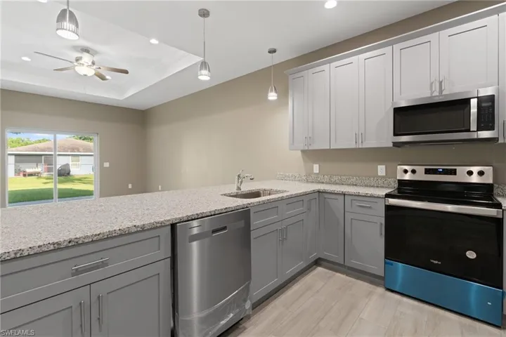 Kitchen featuring ceiling fan, stainless steel appliances, hanging light fixtures, a raised ceiling, and sink