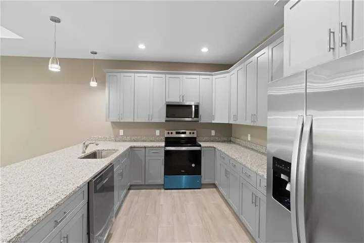 Kitchen featuring stainless steel appliances, hanging light fixtures, sink, light stone countertops, and light hardwood / wood-style flooring