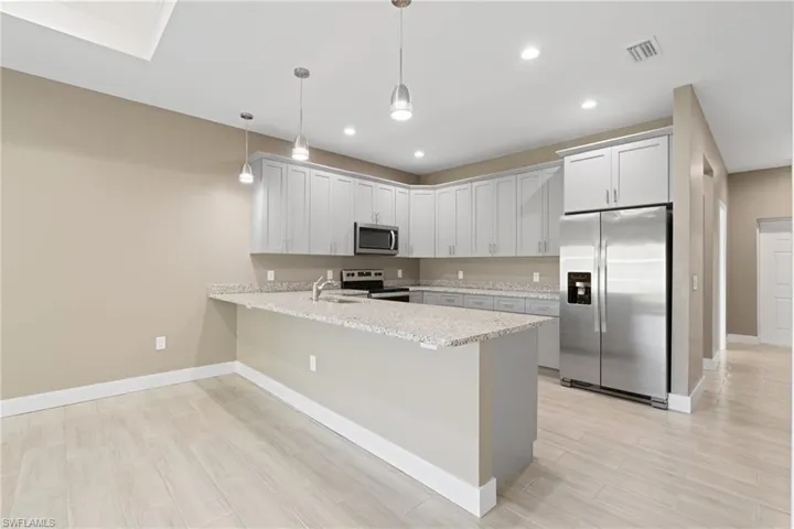 Kitchen featuring hanging light fixtures, white cabinets, light stone countertops, appliances with stainless steel finishes, and kitchen peninsula