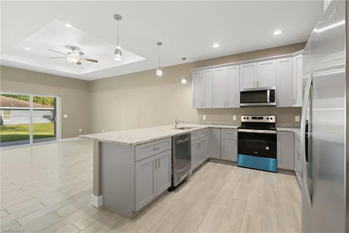 Kitchen with gray cabinets, ceiling fan, a raised ceiling, appliances with stainless steel finishes, and kitchen peninsula