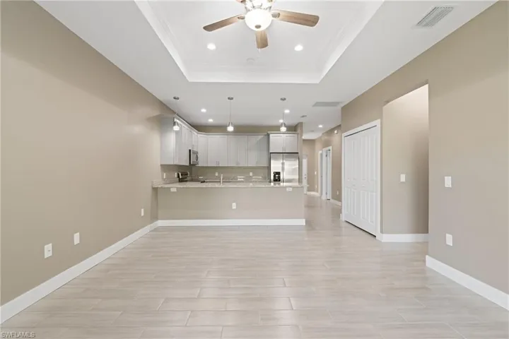 Unfurnished living room featuring ornamental molding, light tile patterned floors, ceiling fan, and a tray ceiling