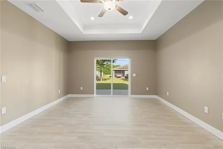 Empty room with ceiling fan, a raised ceiling, and light hardwood / wood-style floors