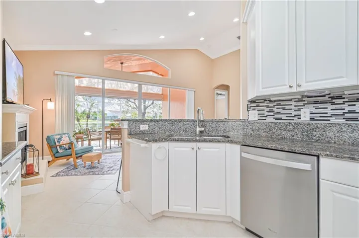 Kitchen with white cabinets, dark stone counters, vaulted ceiling, sink, and dishwasher