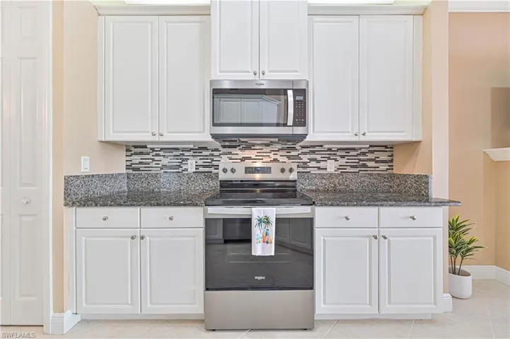 Kitchen with appliances with stainless steel finishes, light tile patterned floors, white cabinetry, and dark stone countertops