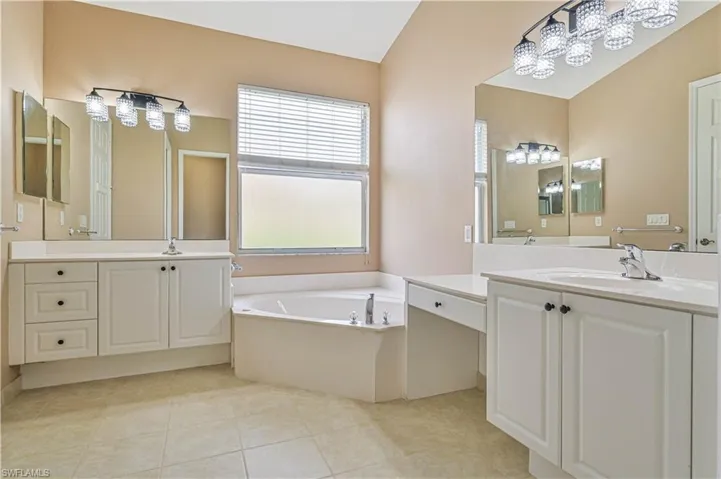 Bathroom featuring tile patterned flooring, vanity, a bath, and vaulted ceiling