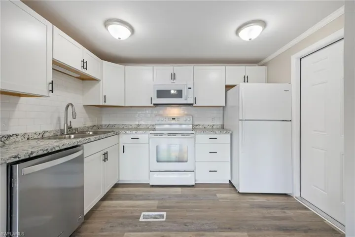 Kitchen featuring white appliances, white cabinetry, dark wood-style flooring, and ornamental molding