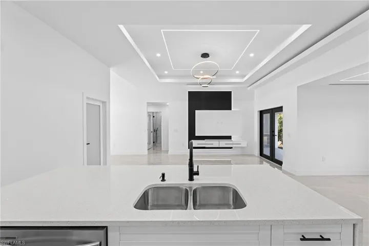 Kitchen featuring a raised ceiling, white cabinetry, light stone countertops, and sink