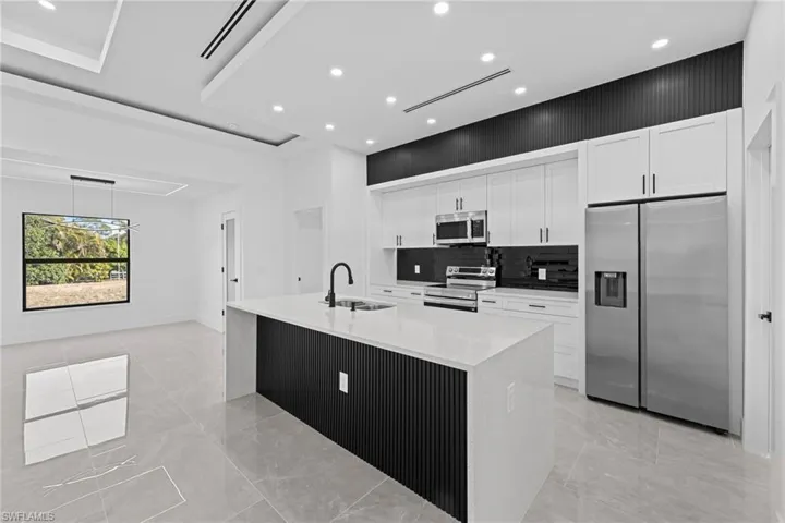 Kitchen featuring sink, appliances with stainless steel finishes, white cabinets, a large island, and backsplash