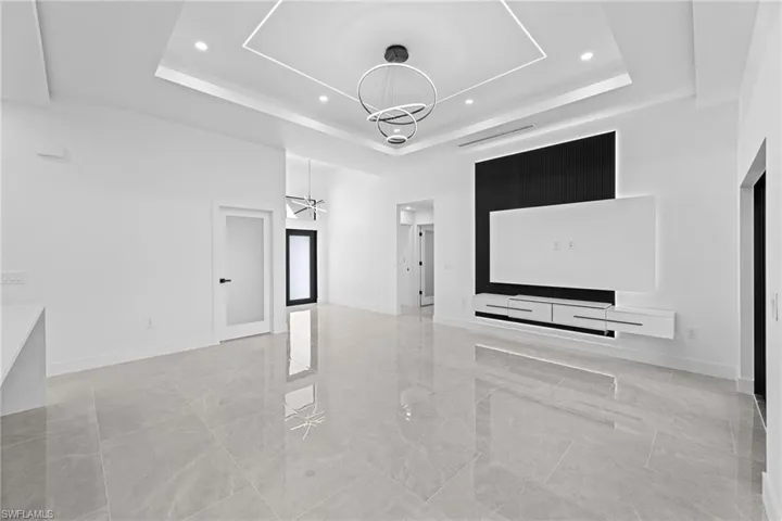 Unfurnished living room featuring a raised ceiling, a chandelier, and a high ceiling