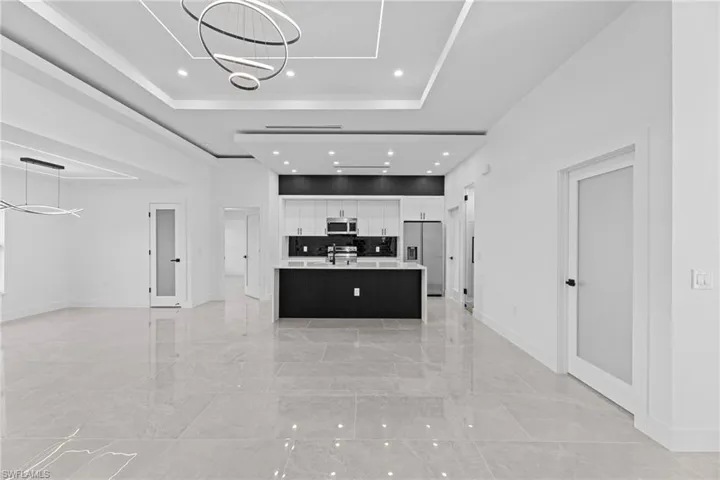 Kitchen featuring pendant lighting, stainless steel appliances, a tray ceiling, an island with sink, and white cabinets