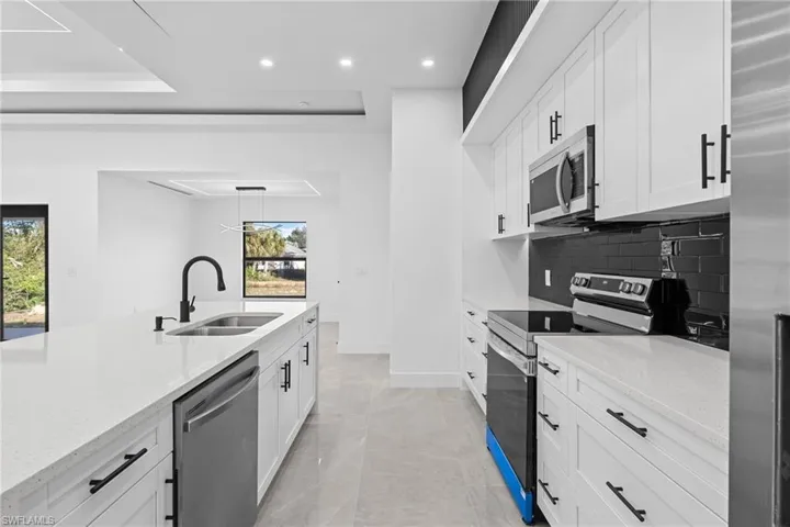 Kitchen with appliances with stainless steel finishes, sink, backsplash, white cabinets, and light stone counters