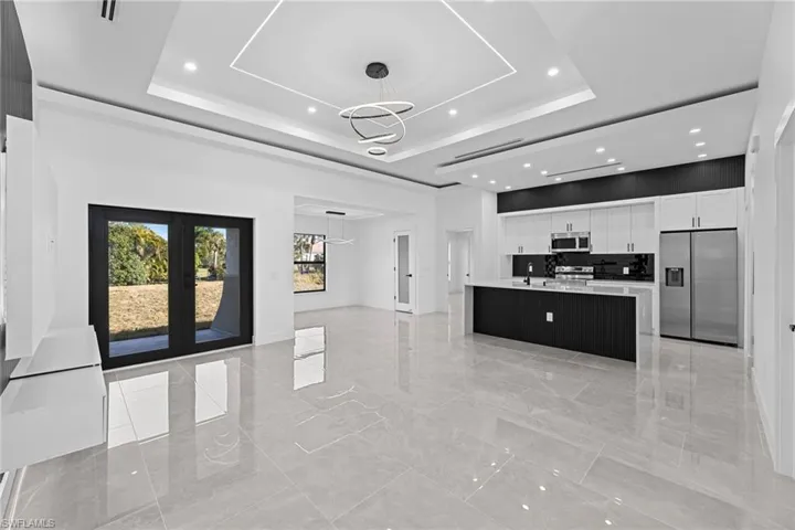 Kitchen featuring appliances with stainless steel finishes, decorative light fixtures, white cabinets, a center island, and a tray ceiling