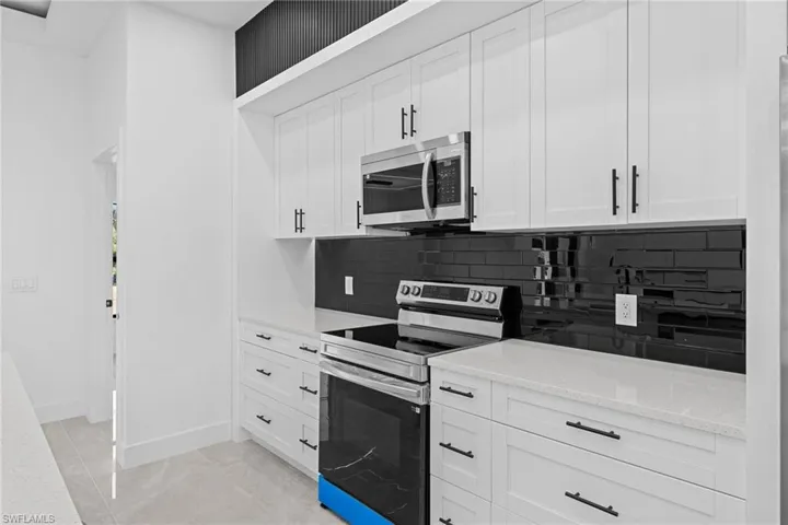 Kitchen with white cabinetry, appliances with stainless steel finishes, and light stone counters