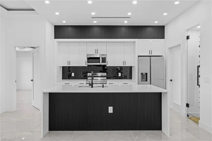 Kitchen featuring sink, white cabinetry, a center island with sink, stainless steel appliances, and backsplash
