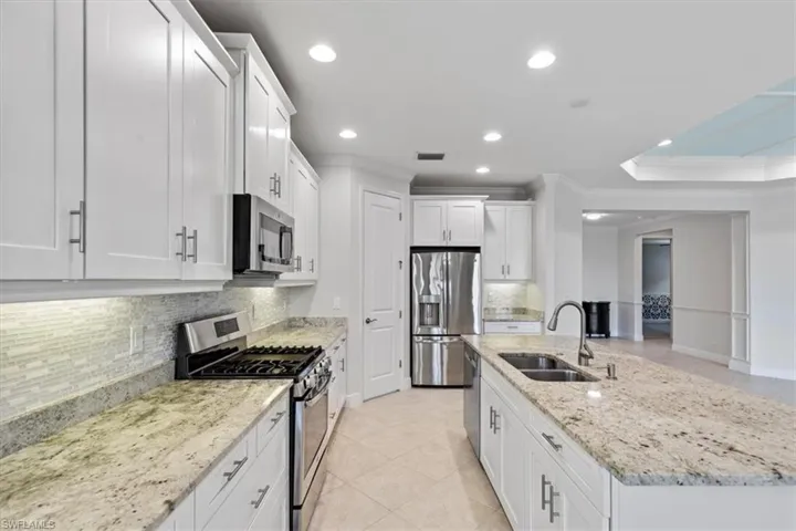 Kitchen featuring appliances with stainless steel finishes, white cabinetry, crown molding, a kitchen island with sink, and sink