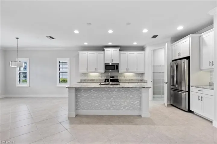 Kitchen with appliances with stainless steel finishes, ornamental molding, white cabinetry, and light stone countertops