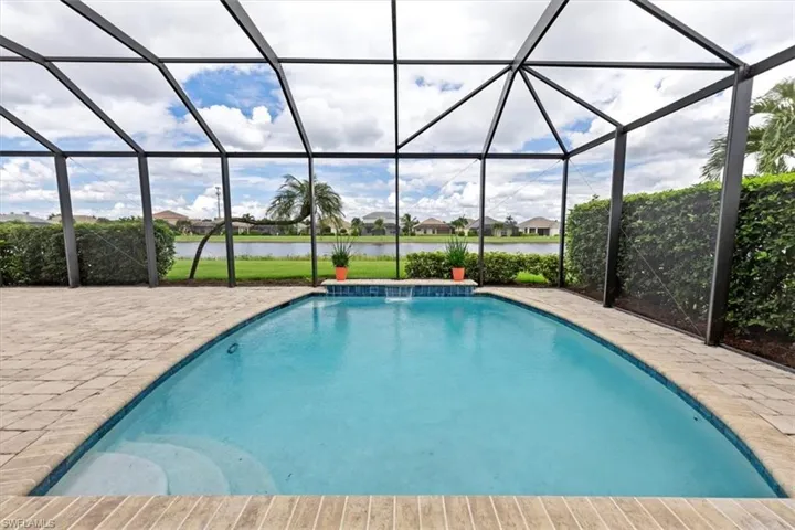View of swimming pool with glass enclosure, a water view, a patio, and pool water feature