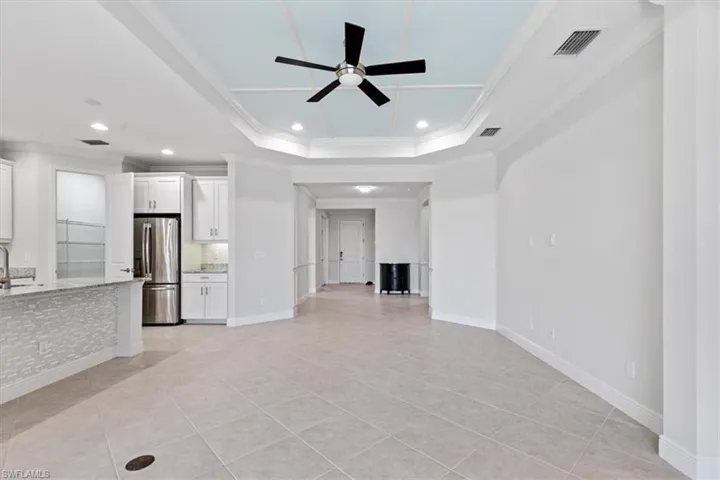 Unfurnished living room featuring light tile patterned floors, a tray ceiling, ornamental molding, and ceiling fan