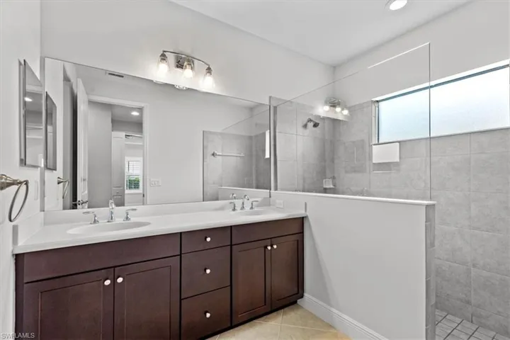 Bathroom featuring a healthy amount of sunlight, tile patterned floors, vanity, and tiled shower
