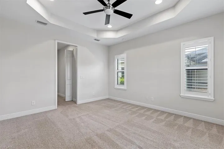 Carpeted spare room featuring ceiling fan and a raised ceiling