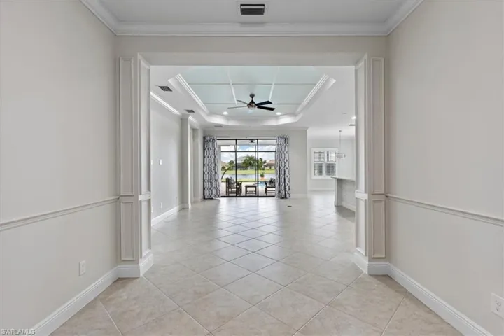 Corridor featuring light tile patterned flooring, ornamental molding, and a tray ceiling