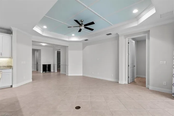 Unfurnished living room featuring ornamental molding, a tray ceiling, ceiling fan, and light tile patterned flooring