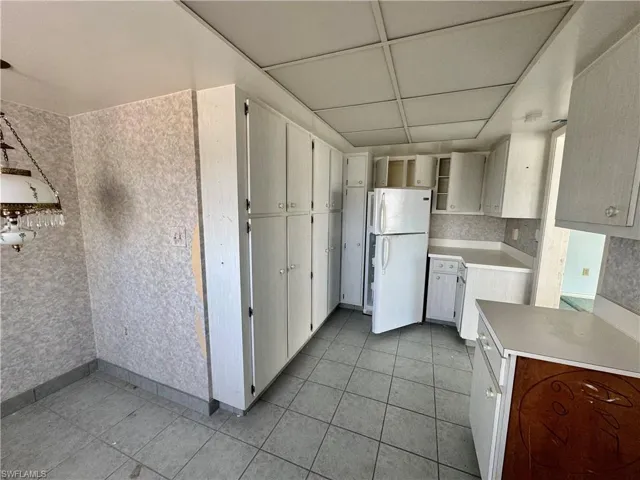 Kitchen with white cabinets, a paneled ceiling, white fridge, and light tile patterned flooring