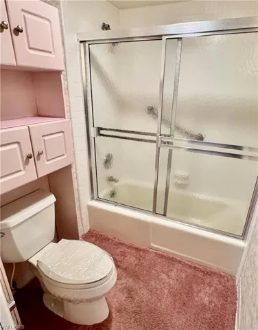 Bathroom with toilet and bath / shower combo with glass door