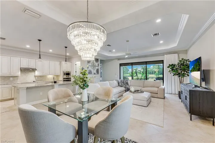 Open-concept living area featuring a large tiered chandelier, tray ceiling with recessed lighting, and expansive sliding glass doors