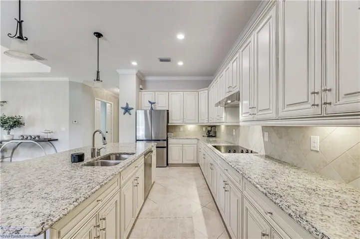 Gourmet kitchen featuring white cabinetry, light granite countertops, stainless steel appliances, a double basin sink, and a tiled backsplash