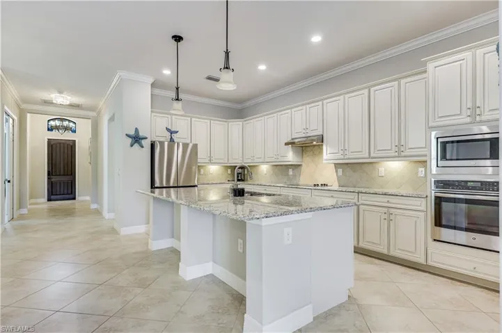 Spacious kitchen featuring an expansive island with granite countertops, abundant white cabinetry, stainless steel appliances, and tile flooring