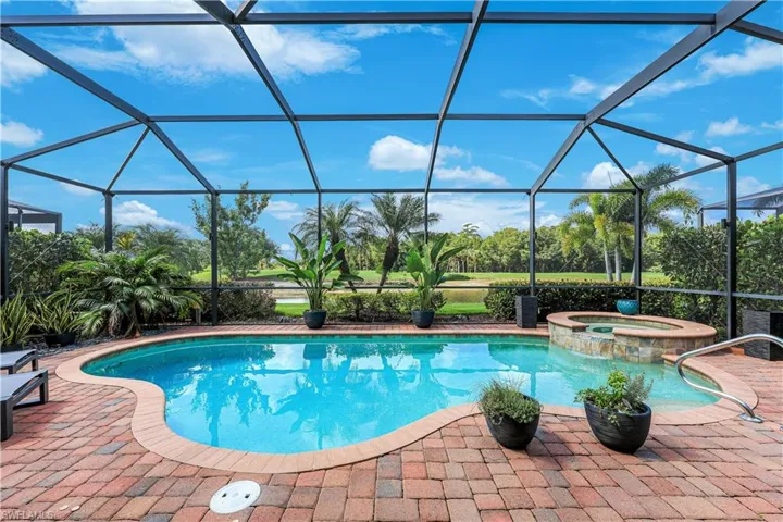 Screened outdoor pool area featuring a freeform pool, integrated spa with stone tile surround, and brick paver decking