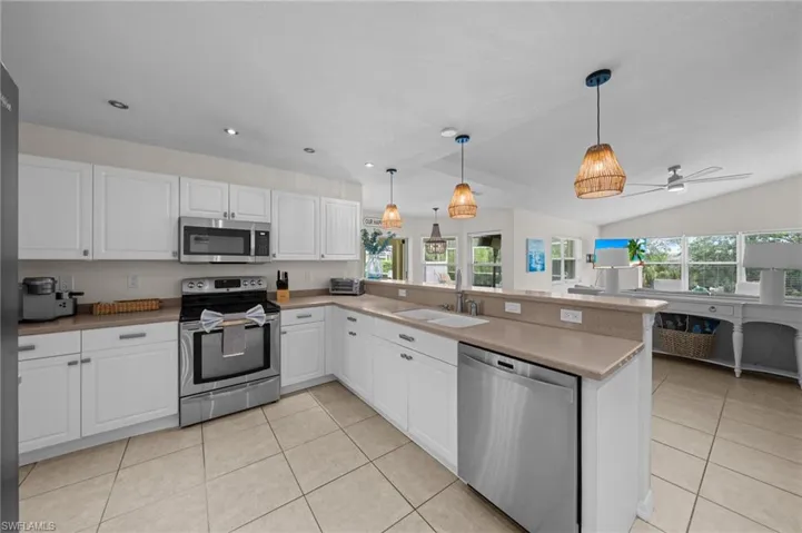 Kitchen featuring appliances with stainless steel finishes, white cabinetry, light tile patterned floors, hanging light fixtures, and a peninsula