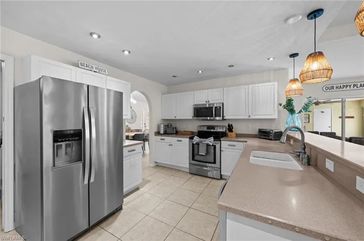 Kitchen featuring appliances with stainless steel finishes, white cabinets, pendant lighting, arched walkways, and light tile patterned flooring