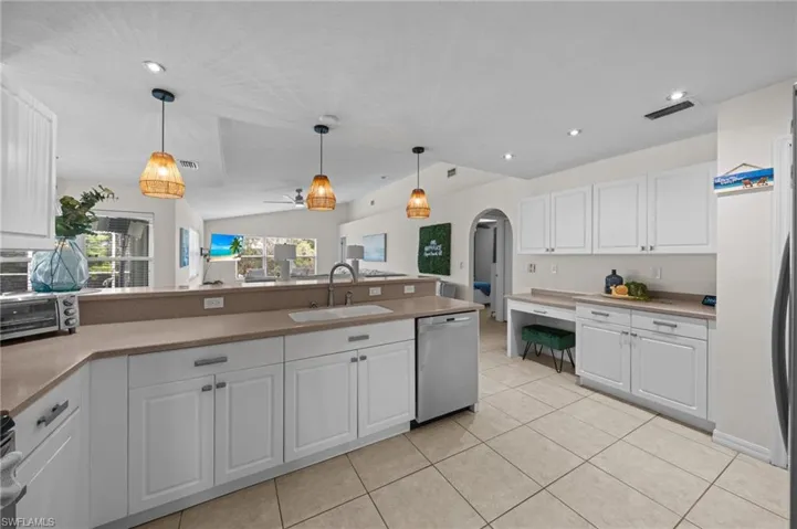 Kitchen with white cabinetry, hanging light fixtures, arched walkways, stainless steel dishwasher, and light tile patterned floors
