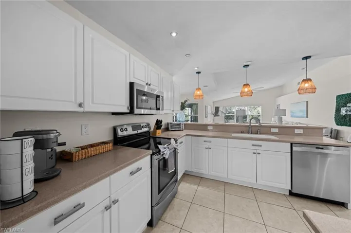 Kitchen with appliances with stainless steel finishes, white cabinetry, pendant lighting, vaulted ceiling, and light tile patterned floors