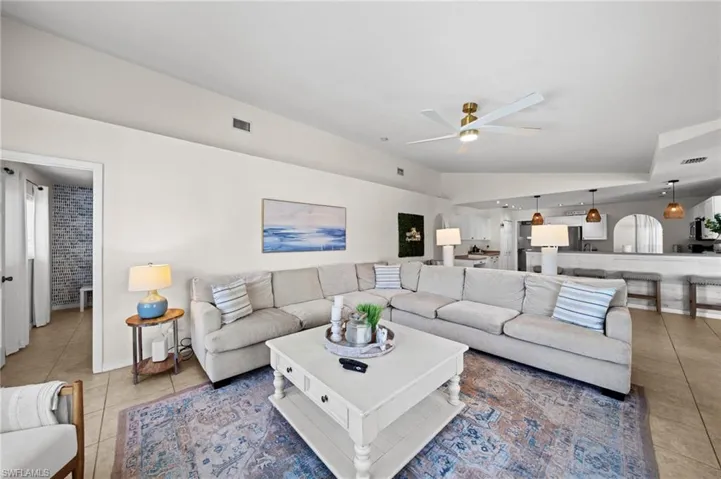 Living room with vaulted ceiling, light tile patterned floors, a ceiling fan, and arched walkways
