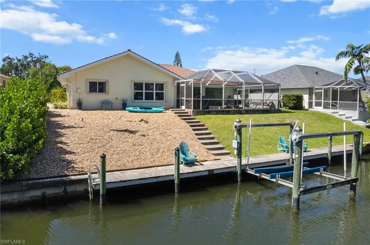Rear view of property featuring a sunroom, stucco siding, glass enclosure, a patio, and boat lift