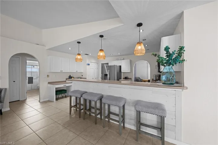 Kitchen featuring arched walkways, a peninsula, a breakfast bar, and white cabinetry