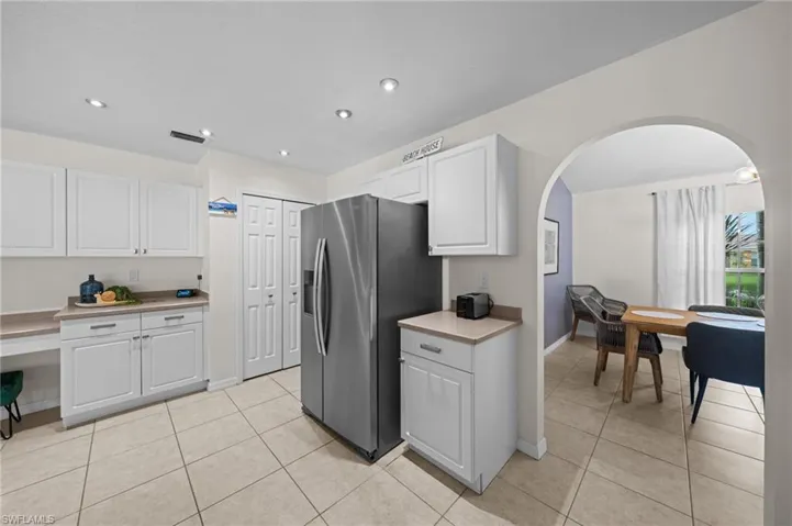 Kitchen featuring light countertops, stainless steel refrigerator with ice dispenser, arched walkways, white cabinets, and light tile patterned floors