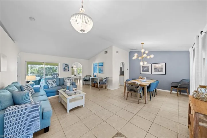Living room featuring vaulted ceiling, a chandelier, arched walkways, and light tile patterned floors