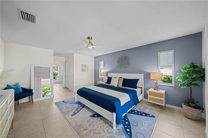 Bedroom featuring light tile patterned floors, multiple windows, a ceiling fan, and ensuite bath