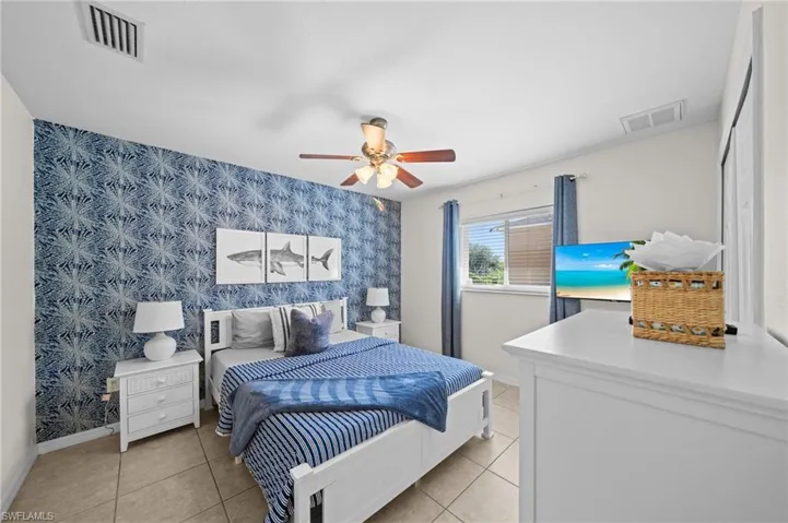 Bedroom featuring wallpapered walls, light tile patterned floors, ceiling fan, and an accent wall